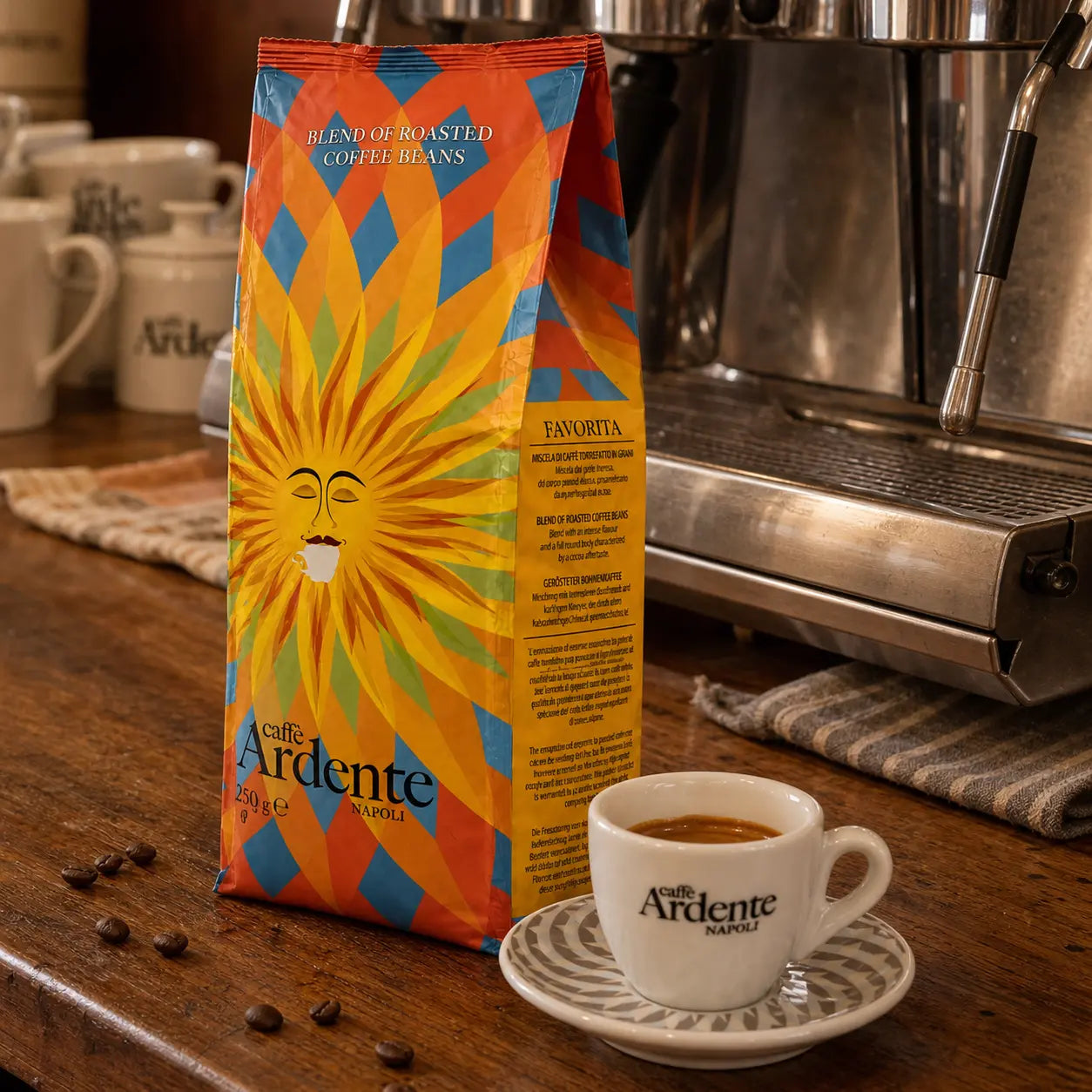 Caffè Ardente Favorita, 250g Kaffeebohnen in orange-blau-gelber Sonnenmotiv-Verpackung, mit Espressotasse an der Siebträgermaschine