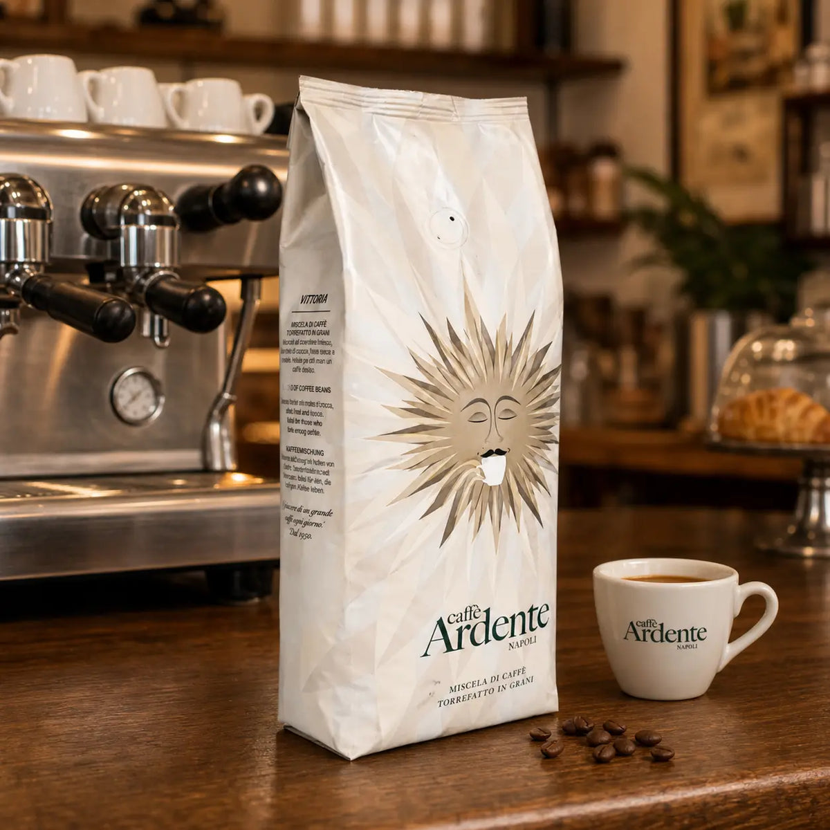 Caffè Ardente Vittoria Kaffeebohnen in cremeweißer Sonnenmotiv-Verpackung, mit Espressotasse auf Holztheke im Café