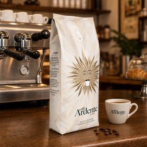 Caffè Ardente Vittoria Kaffeebohnen in cremeweißer Sonnenmotiv-Verpackung, mit Espressotasse auf Holztheke im Café