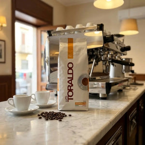 Caffè Toraldo Linea Arancio, Kaffeebohnen-Packung mit zwei Espressotassen und losen Bohnen auf Marmortheke im Café