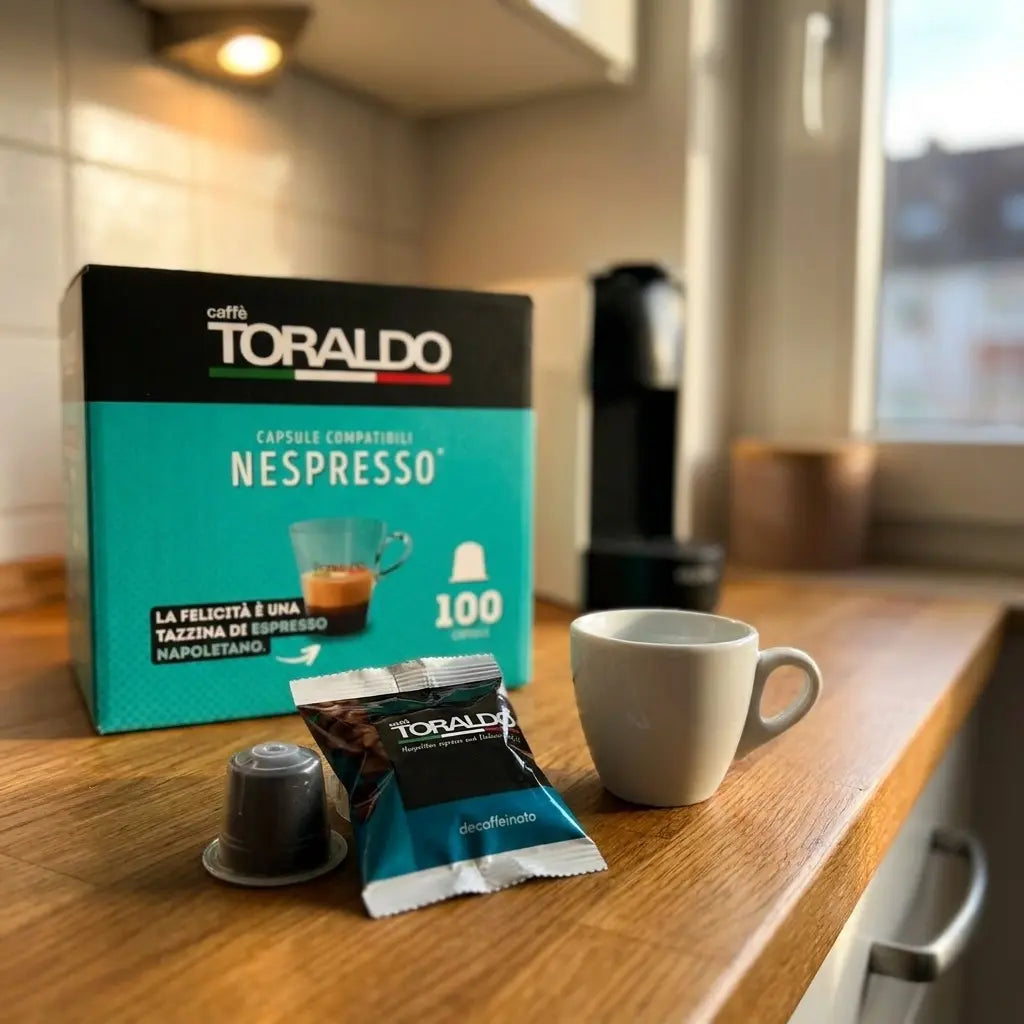 Caffè Toraldo Nespresso-kompatible Kapseln Decaffeinato, 100er-Packung mit Espressotasse und Kapsel vor Nespresso-Maschine
