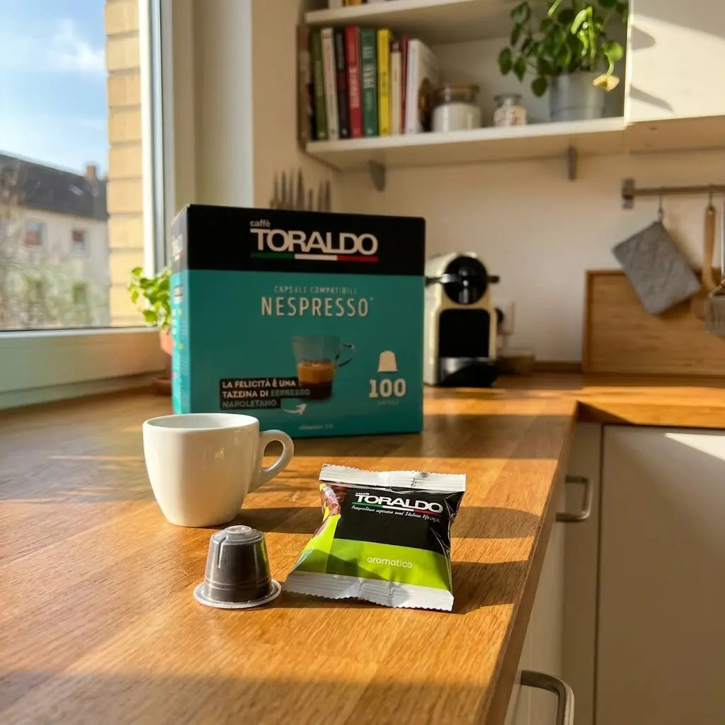 Caffè Toraldo Nespresso-kompatible Kapseln Aromatico, 100er-Packung mit Espressotasse und Kapsel vor Nespresso-Maschine