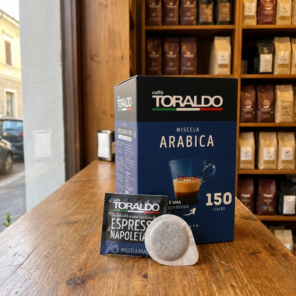 Caffè Toraldo Miscela Arabica, 150 ESE-Pads-Packung mit einzelnem Pad-Beutel und Kaffeepad auf Holztheke im Ladengeschäft